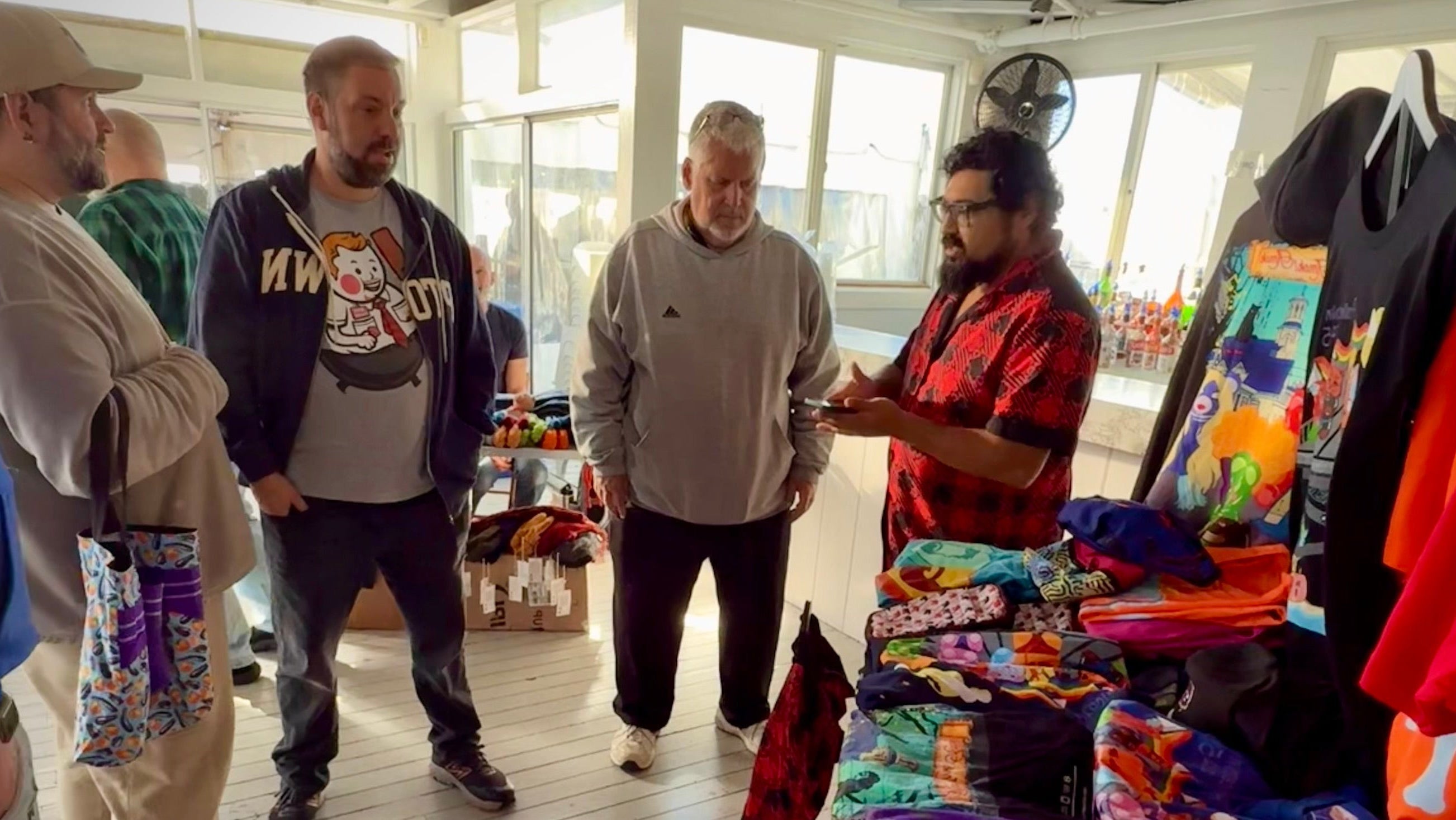 People shopping for colorful clothing on a wooden deck with large windows.
