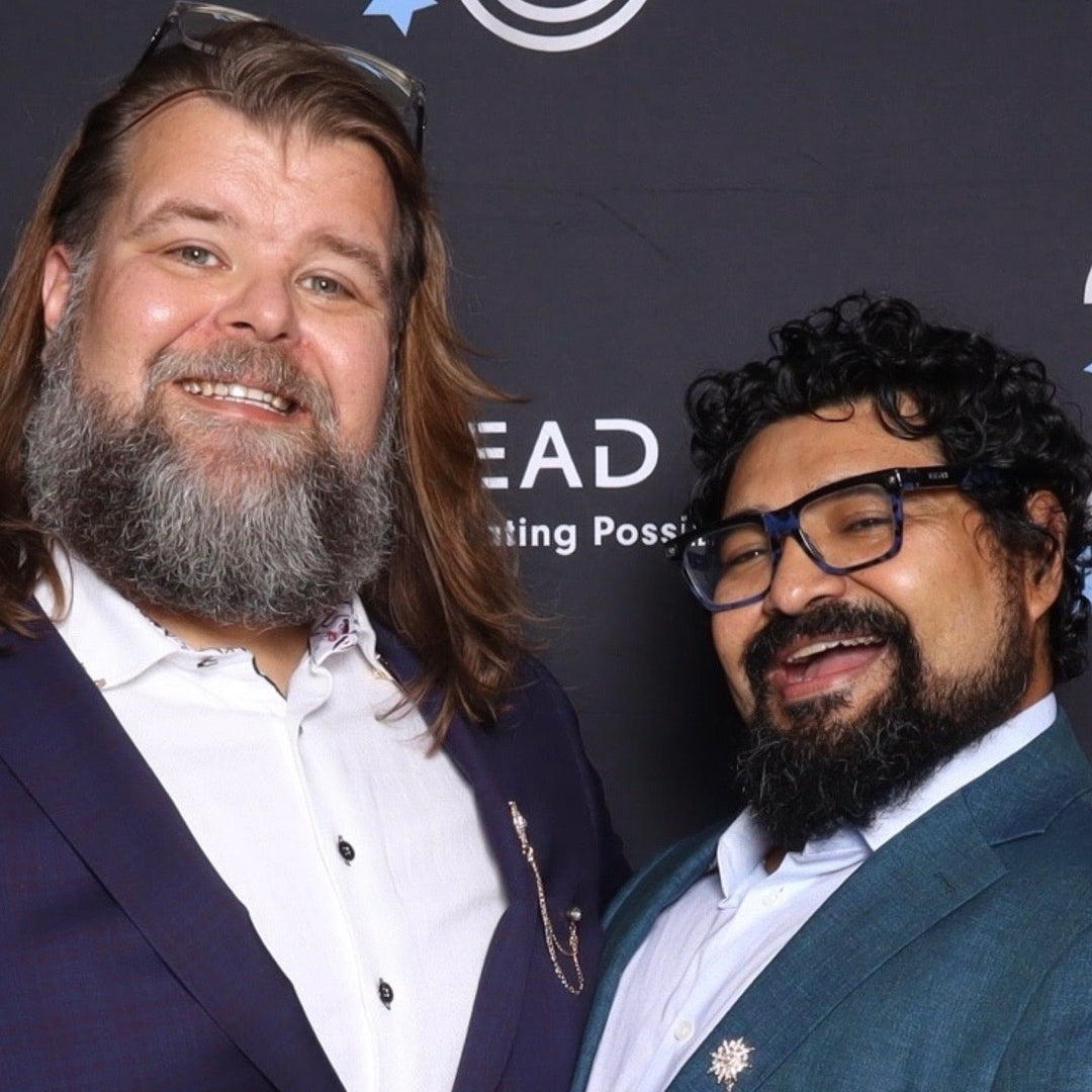 Two men in suits standing in front of a Callen-Lorde 25th anniversary backdrop.