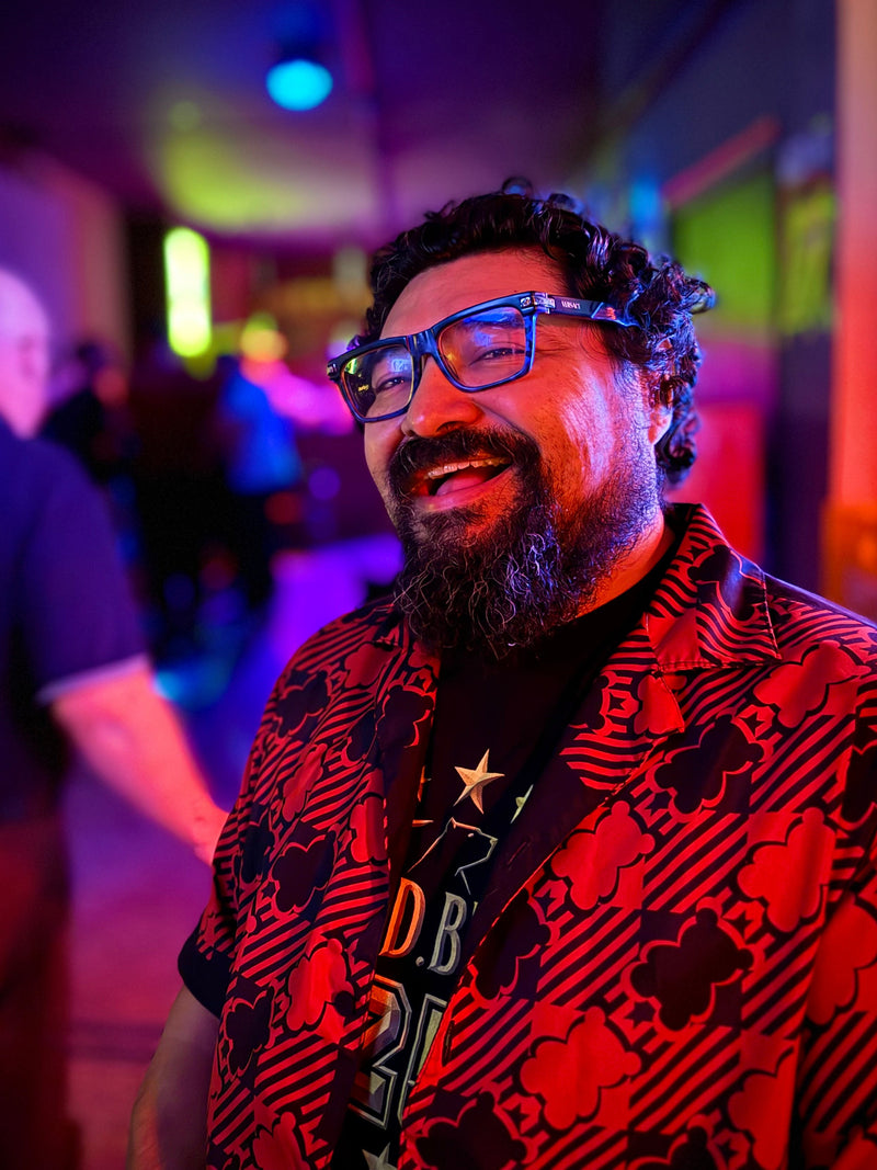 Man wearing glasses and a patterned shirt in a dimly lit room with colorful lighting