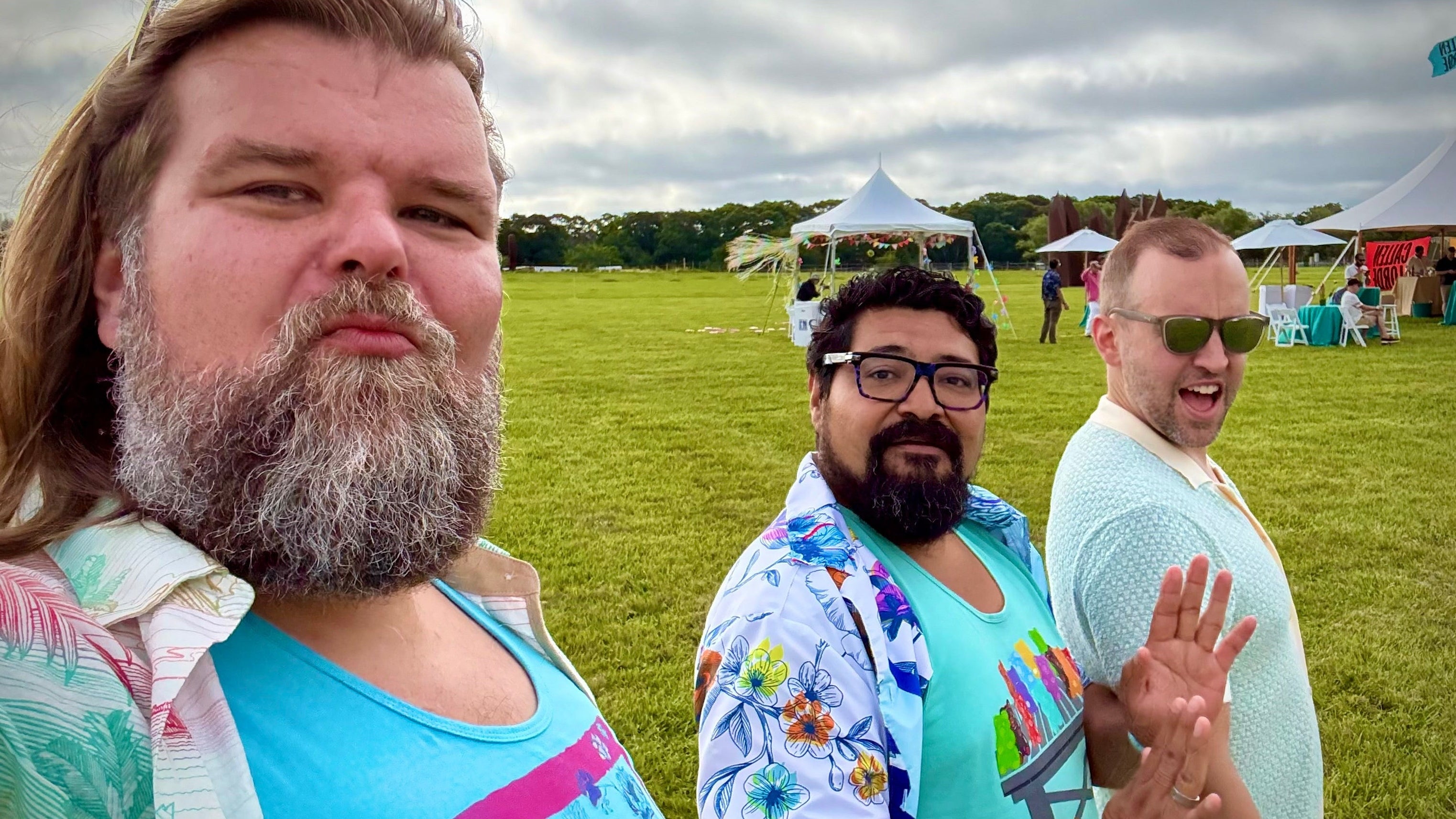 Three men standing in a grassy field with tents in the background