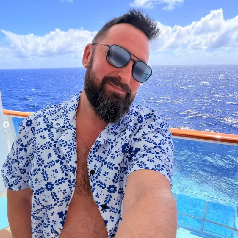 Man with sunglasses and a floral shirt on a cruise ship deck with ocean view